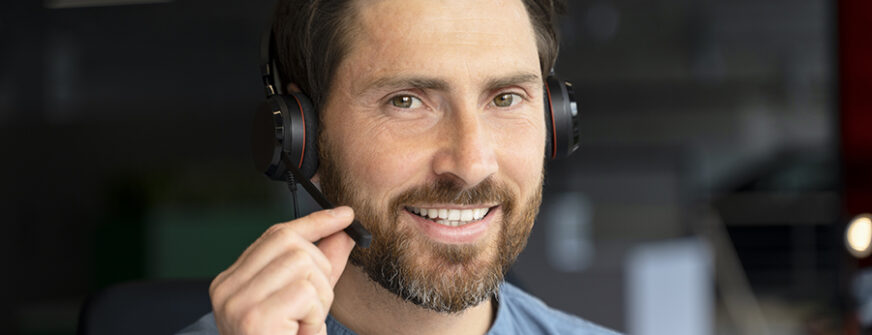 Businessman is smiling while adjusting his headset microphone during his workday